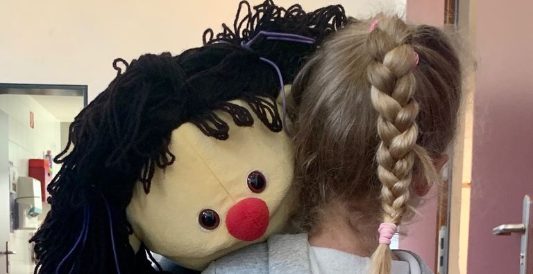 Kind trägt eine große Mädchen Klappmaulpuppe über der Schulter Kinder- und Jugendtherapie